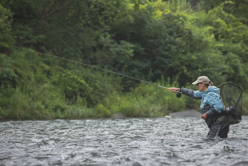 An angler casts into a fast-flowing stream.