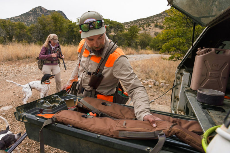 A hunter in a midweight shooting shirt looks through his gear.