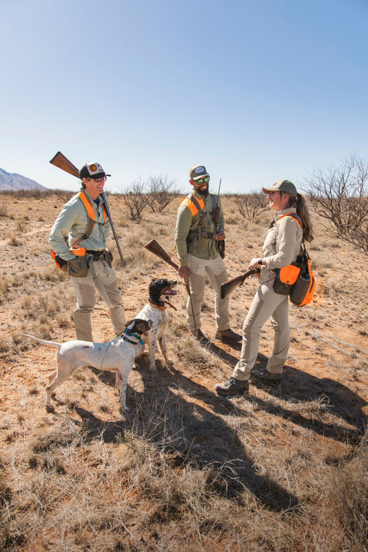 A group of hunters gather around a sitting dog on the prairie.