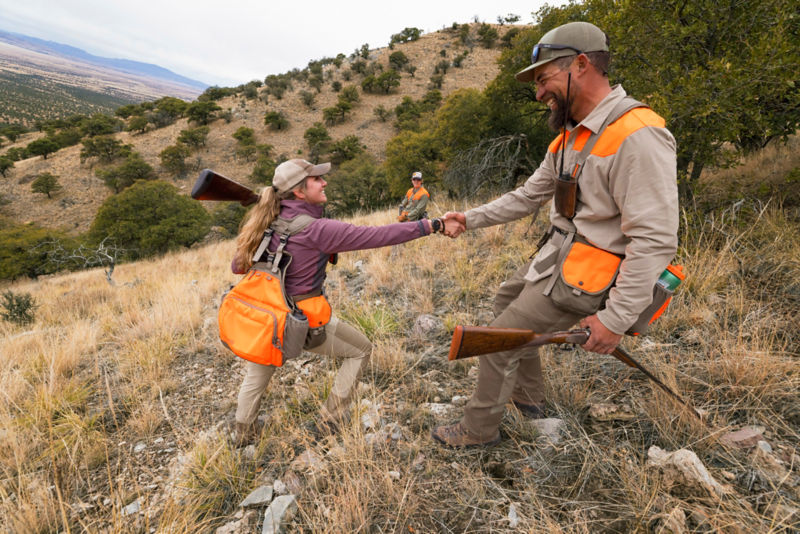 A group of hunters helps each other up a steep rocky hillside.