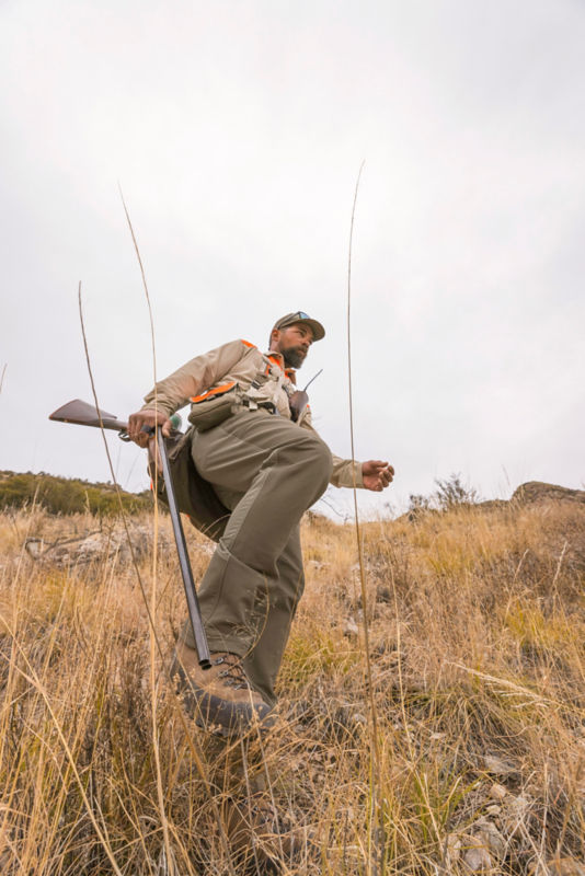 Men's PRO upland softshell pants scrambles down a rocky hill.