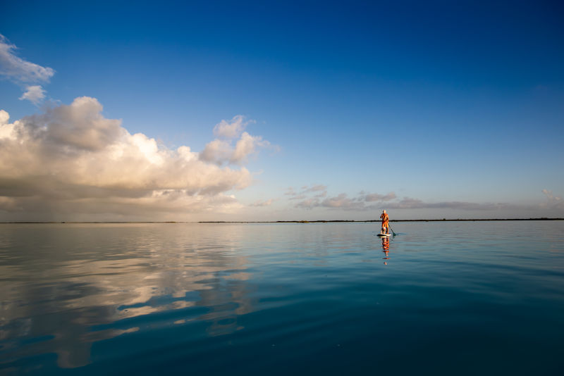 A paddleboarder on a still ocean with a small child.