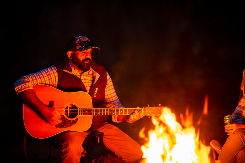 A guitarist playing around the campfire.