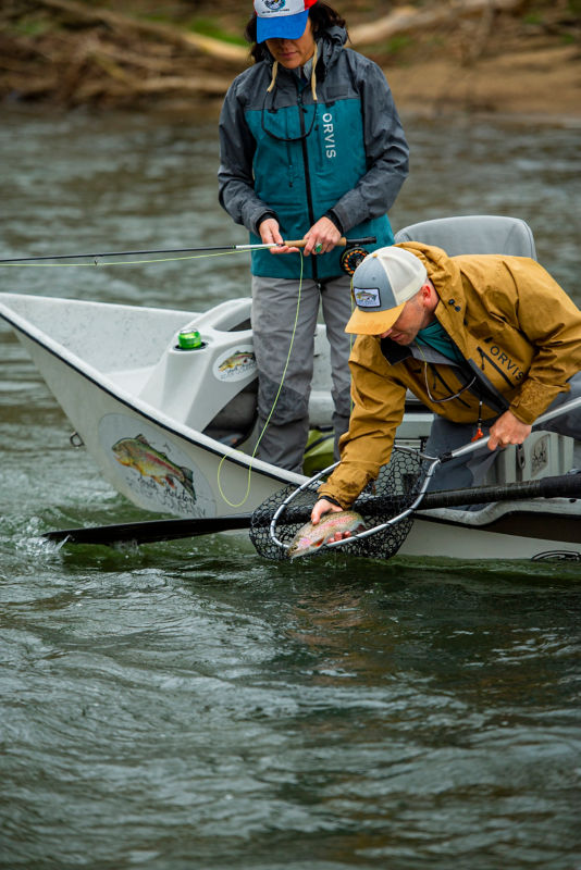 A fishing guide releasing an angler's fish from a drift boat.