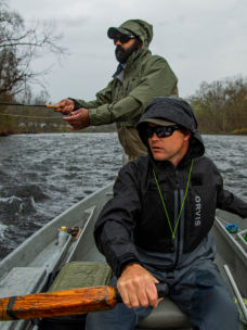 Two people in a small boat; one person is fly fishing while the other person rows.