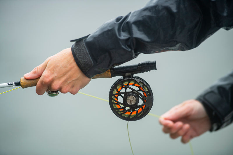 Two hands holding a fly-fishing rod while fishing.