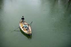 Two anglers cast from either end of a boat on the river.