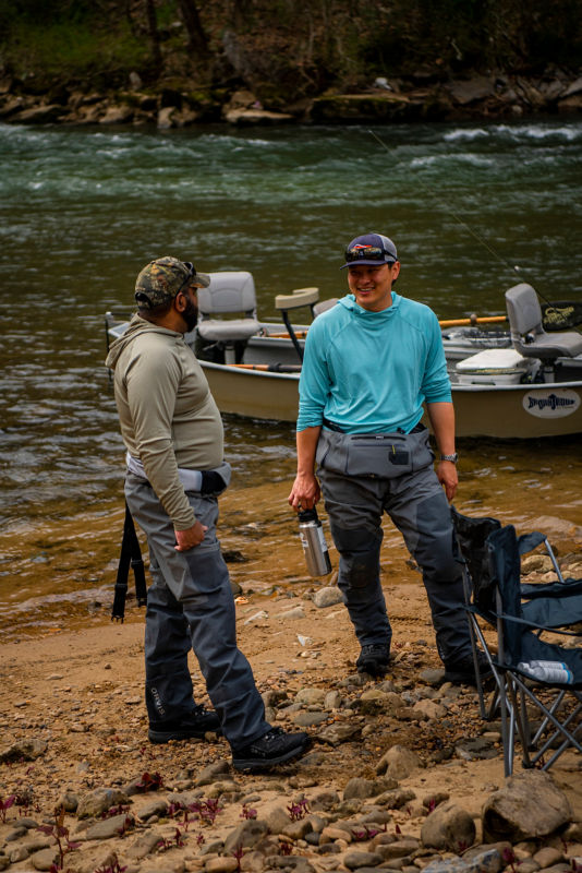 Two friends in fly-fishing gear catching up by a river.