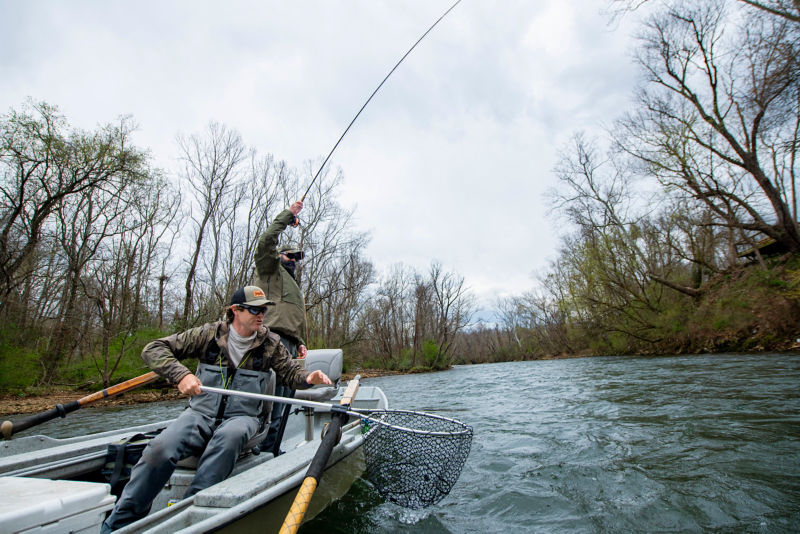 Two anglers in a boat reeling in a fish.