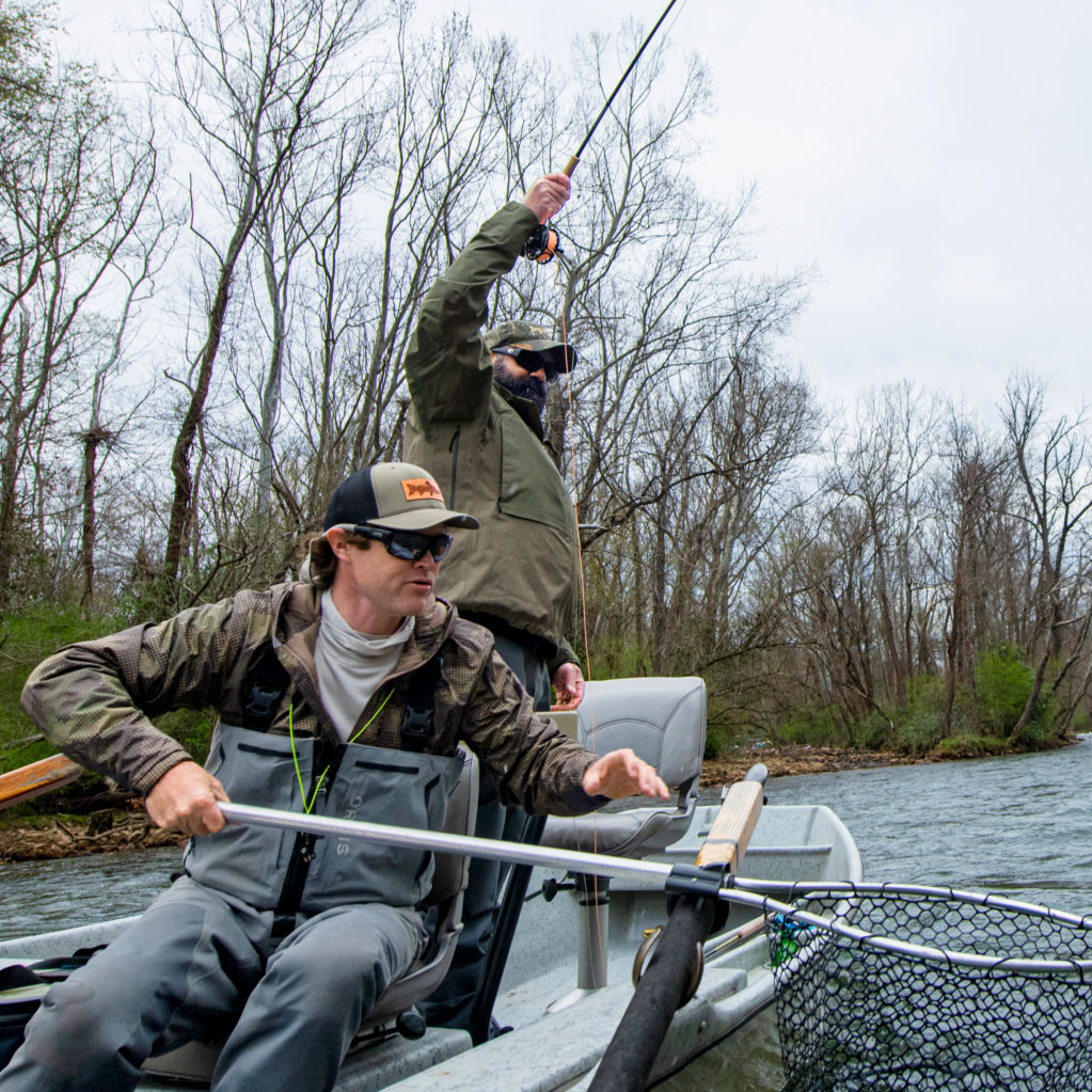 Two anglers in a boat reeling in a fish