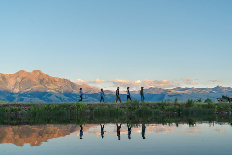 A group hikes across a field single file with mountains in the background.