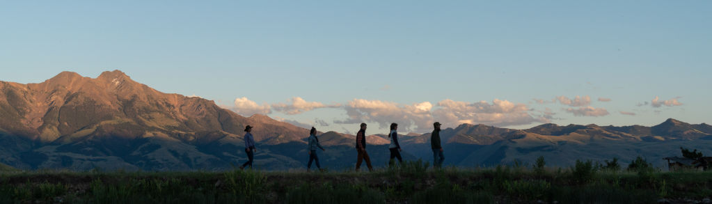 A group hikes single file with mountains in the background