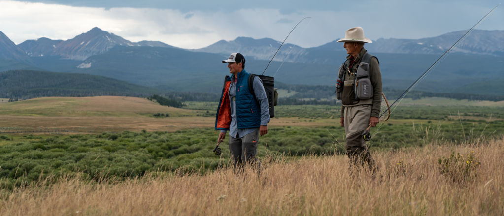 Son and father walking across a field in Montana with fishing gear.