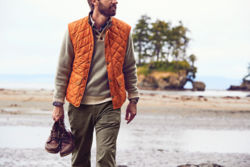 Man in orange vest holding a pair of boots on a beach
