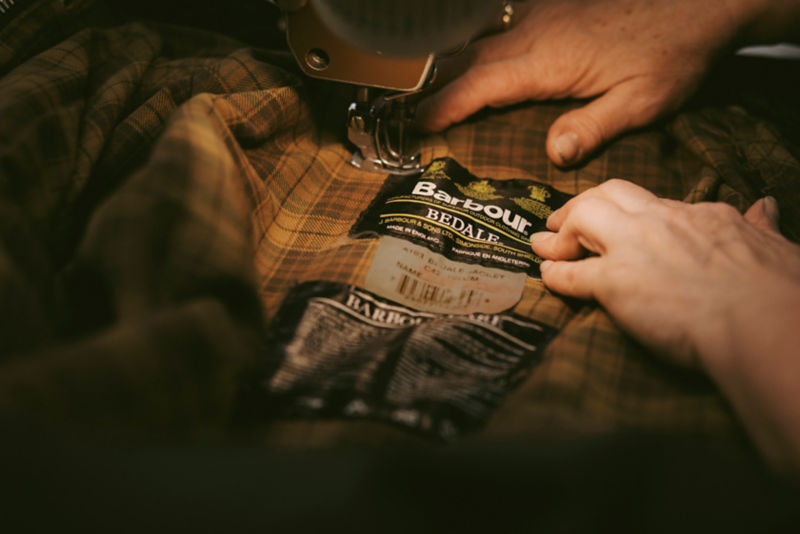 Close-up of someone sewing the interior lining of a Barbour jacket.