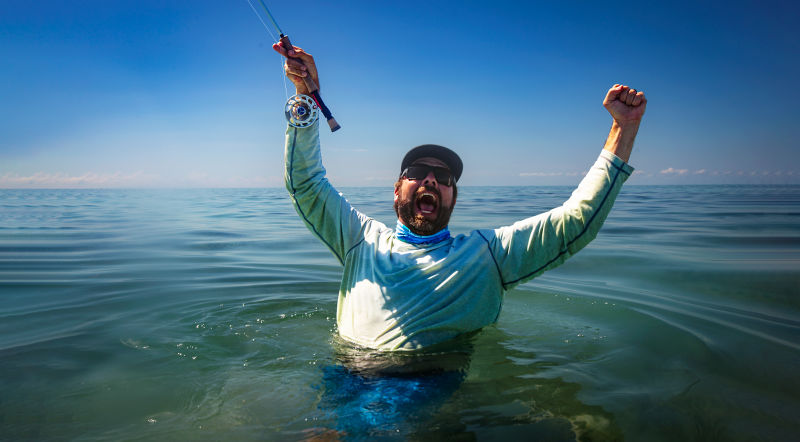 An angler celebrates a catch from waist-deep in turquoise waters.