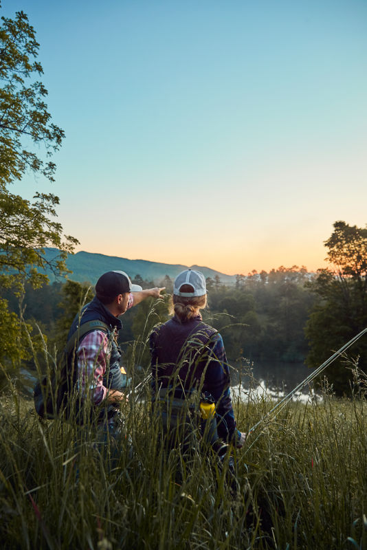 Anglers with their gear push through brush at dawn.