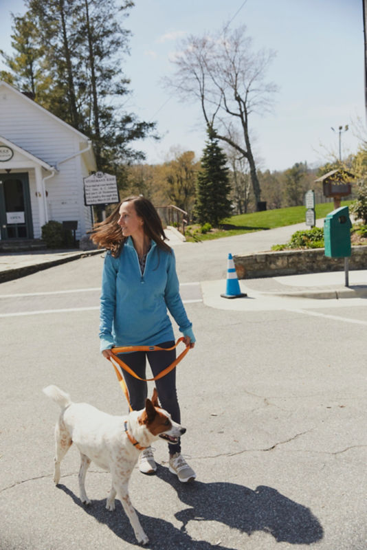 A woman wearing a blue zipneck sweatshirt walking her dog on an orange leash