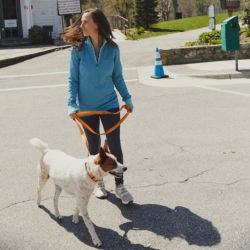 A woman wearing a blue zipneck sweatshirt walking her dog on an orange leash