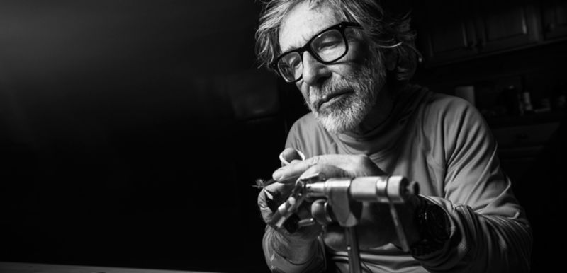 A black and white headshot of Tom Rosenbauer tying a fly.