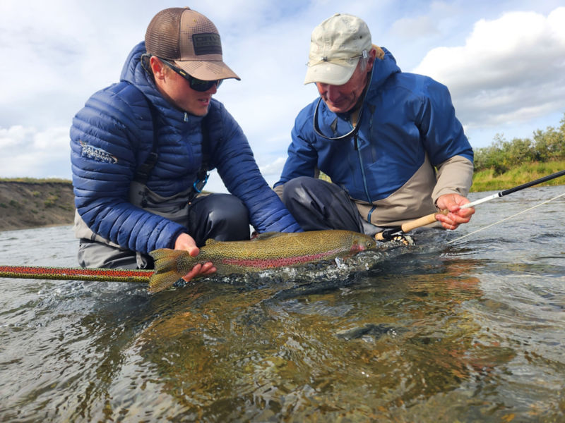 Two anglers release a rainbow trout back into the water.