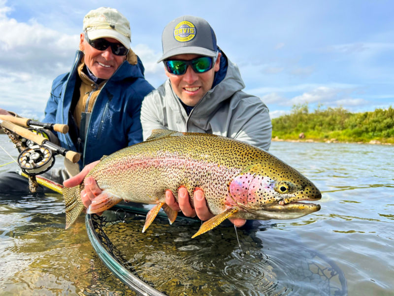 Two men in fishing gear holding a large fish toward the camera.