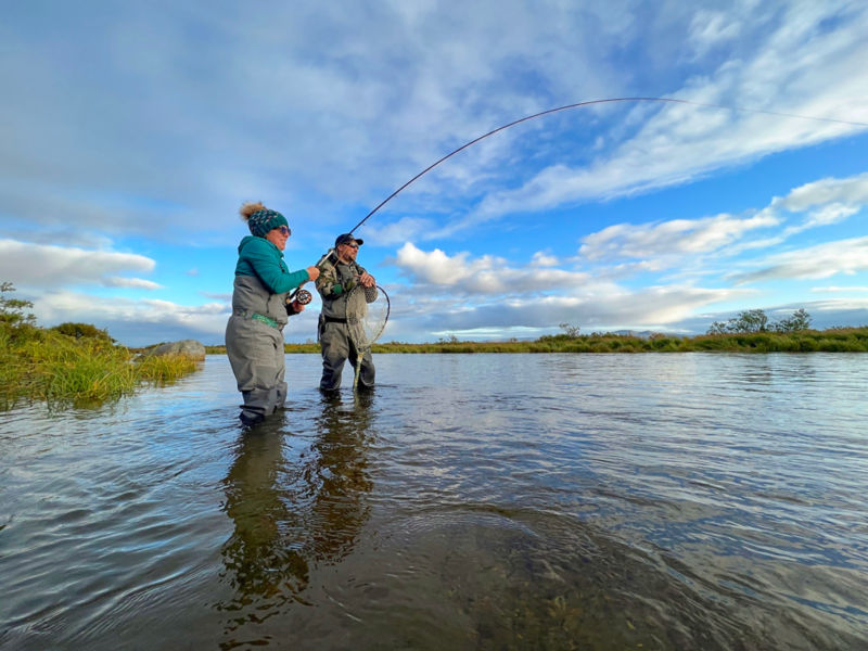 An angler lands a fish in a net wielded by another angler.