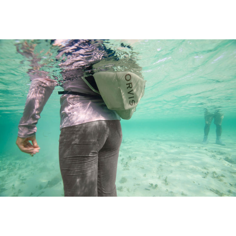 An angler with a hip pack standing chest-deep in clear turquoise water