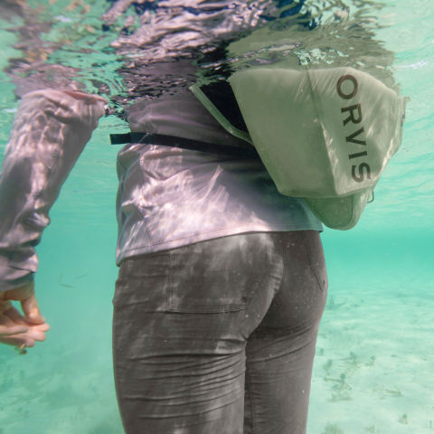 An angler with a hip pack standing chest-deep in clear turquoise water