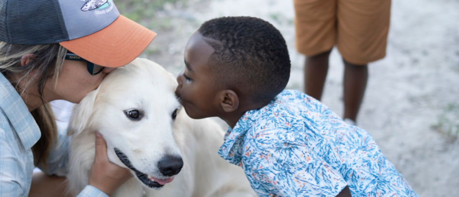 A young boy kissing a calm white dog