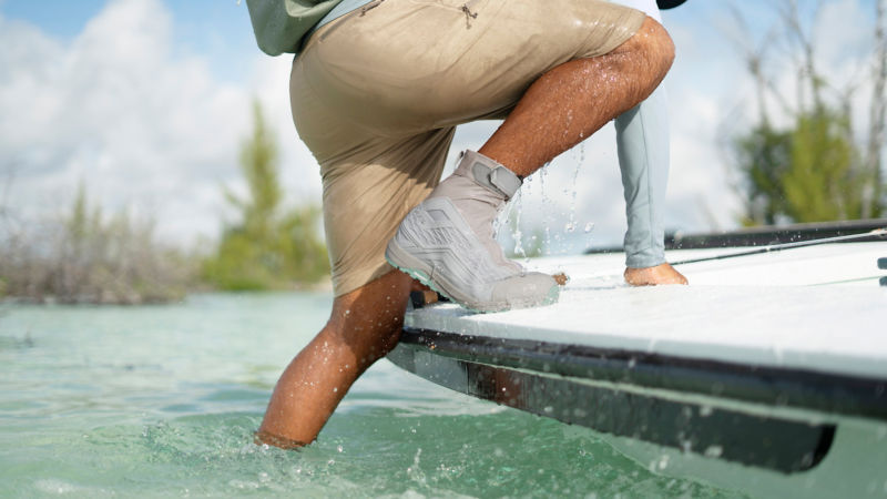 A wading boot as the angler wearing it steps out of the water into a boat