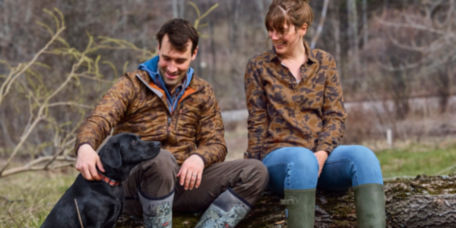 Charley and Hannah Perkins sitting on a log next to a black Labrador Retriever
