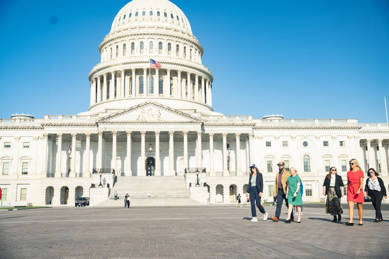 A group of people walk by the front of the US Capitol.