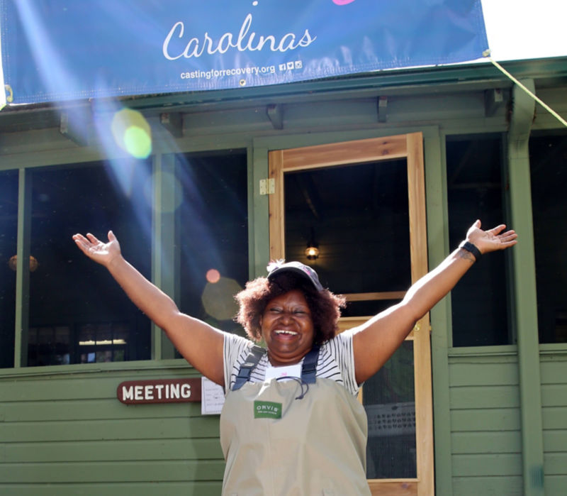 A woman in front of building with CFR banner with her arms raised in celebration.