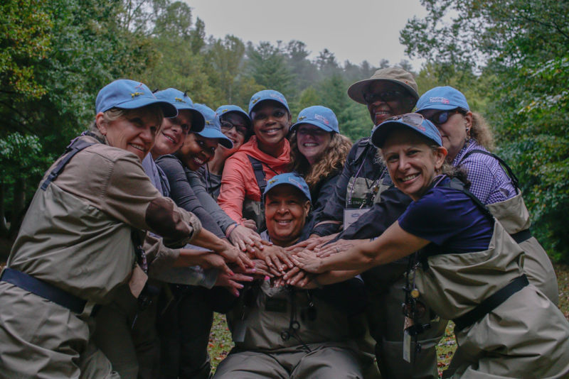 A group of women in angling gear with hands stacked in the middle.