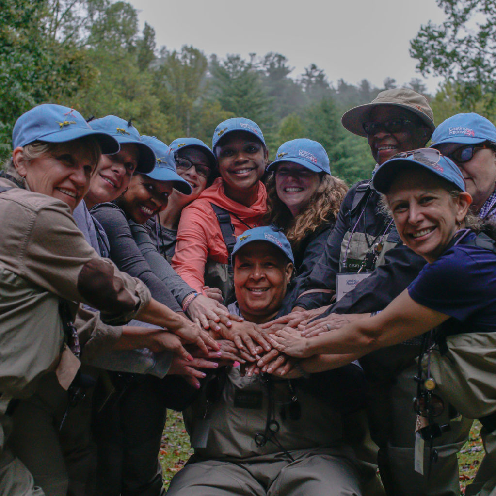 A group of women in angling gear with hands stacked in the middle