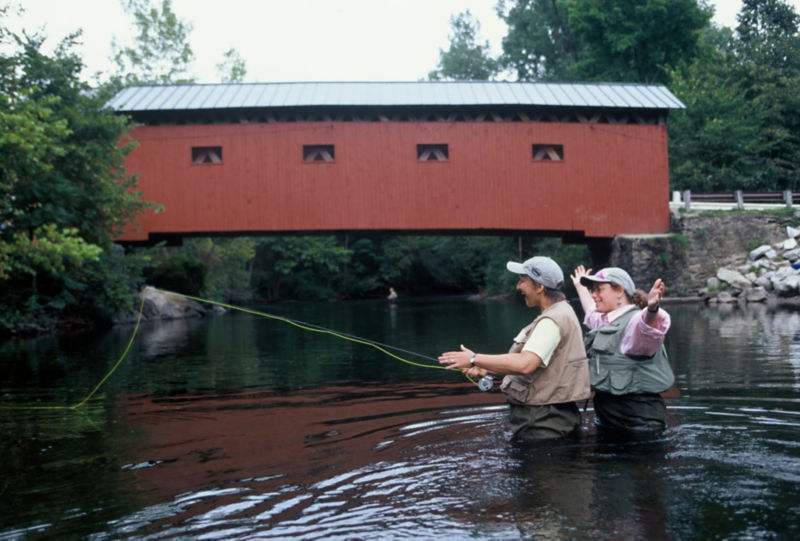 Celebrating 25 years Casting for Recovery 1996-2021, two people fishing by a covered bridge.