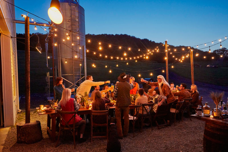 Family and friends gather around an outdoor table lit up by fairy lights.
