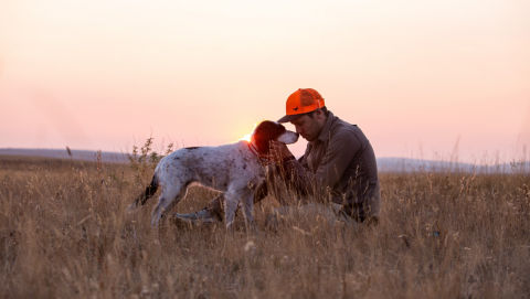 Simon Perkins with his dog Copa in a field of dry grass at sunrise.