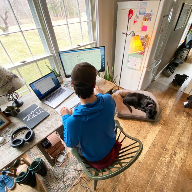 A man at his desk in his home office next to his dog asleep in a dog bed