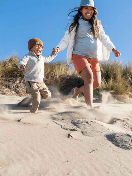 Woman in Open-Air Caster Hoodie runs down a sand dune with her child.