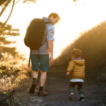A man and his child walk up a rocky path at sunset.