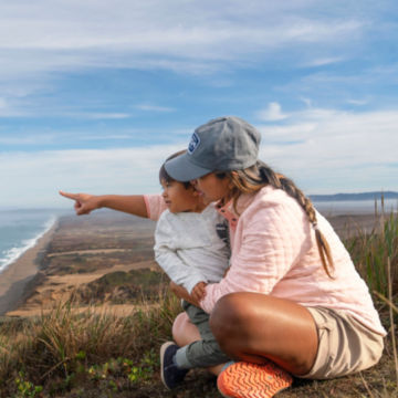 Woman in Outdoor Quilted Sweatshirts overlooks the ocean with her child.