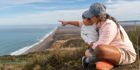 A mother holds her son in her lap while they look over the ocean.