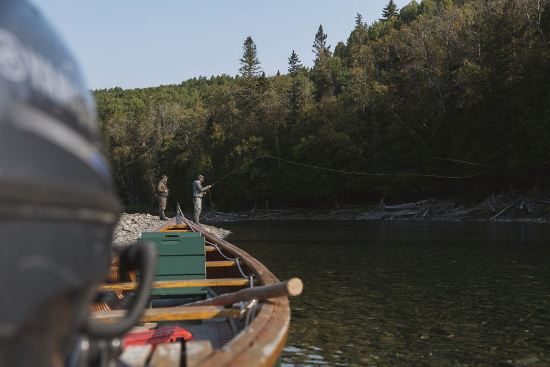 An angler casts their fly rod from the gravel bank of a river.