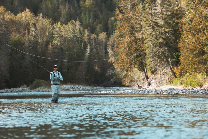 An angler swings his rod from calf-deep in a river.
