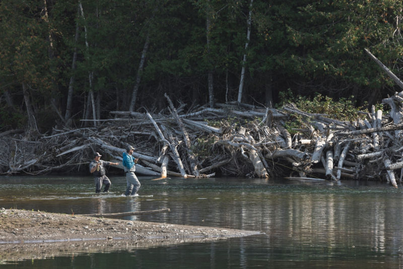 A guide instructs an angler in their cast on a rocky river.