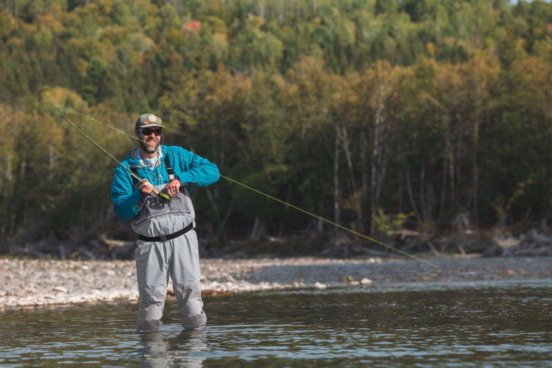 A smiling angler wearing waders sets a hook on the river.