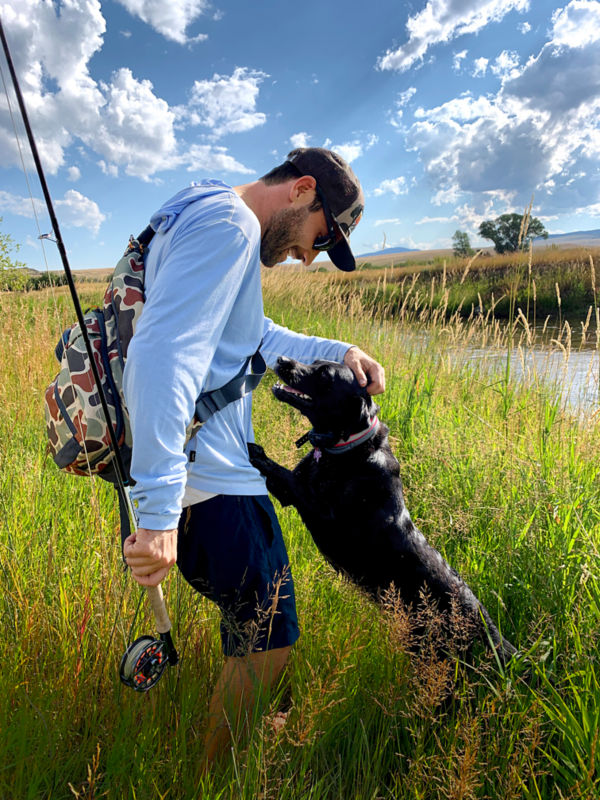 Charley standing in a grassy field with his rod petting his black lab.