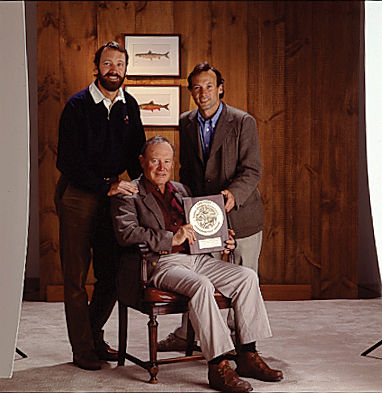 Leigh is sitting down, holding an award, with his sons Dave and Perk standing behind him.
